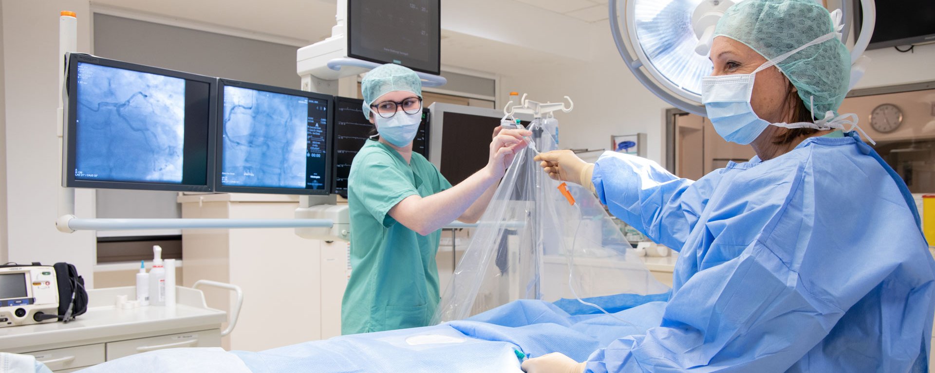 Im Operationssaal des Herz- & Gefäßzentrums Kempten-Oberallgäu stellen zwei Teammitglieder in OP-Kleidung die Versorgung des Patienten sicher